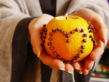 Žena drží svícen z pomeranče se zapíchaným hřebíčkem